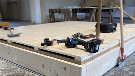 Verschlossenes Holzbauelement in der Werkhalle; auf der Deckplatte liegen Akkuschrauber, Hammer und weiteres Handwerkzeug.