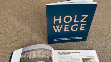 Ausstellungskatalog „HOLZWEGE“ mit aufgeschlagenen Seiten zu zeitgenössischem Holzbau.