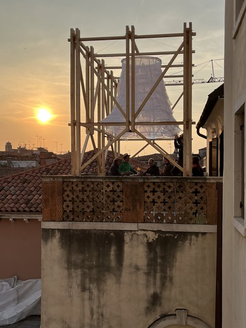 Gerüst mit einem großen, weißen, glockenförmigen Objekt auf einem Balkon bei Sonnenuntergang