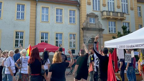 Menschenmenge vor einem historischen Gebäude mit Protestschildern und einem Zelt mit der Aufschrift 'OMAS GEGEN RECHT'