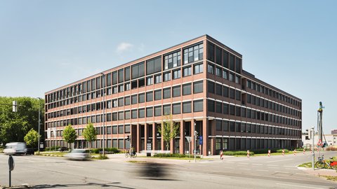 Großes mehrstöckiges Bürogebäude mit rotem Backstein und vielen Fenstern an einer Straßenkreuzung bei Tageslicht