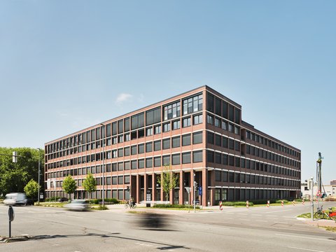 Großes mehrstöckiges Bürogebäude mit rotem Backstein und vielen Fenstern an einer Straßenkreuzung bei Tageslicht