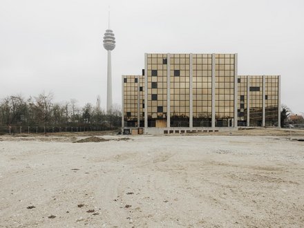 Außenansicht eines Schulgebäudes mit goldfarbener Rasterfassade auf freiem Gelände, Fernsehturm im Hintergrund.