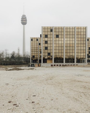 Außenansicht eines Schulgebäudes mit goldfarbener Rasterfassade auf freiem Gelände, Fernsehturm im Hintergrund.