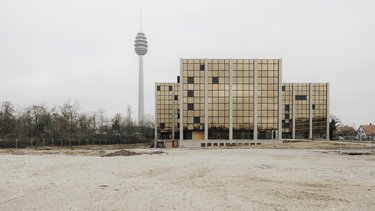 Außenansicht eines Schulgebäudes mit goldfarbener Rasterfassade auf freiem Gelände, Fernsehturm im Hintergrund.