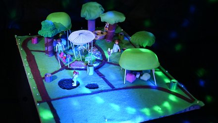 Modell eines grünen Parks mit Wegen, Pavillon und spielenden Figuren.