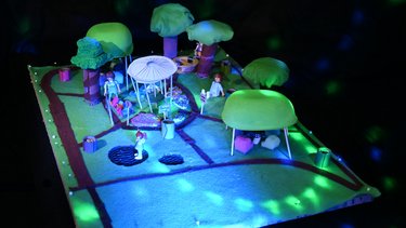 Modell eines grünen Parks mit Wegen, Pavillon und spielenden Figuren.