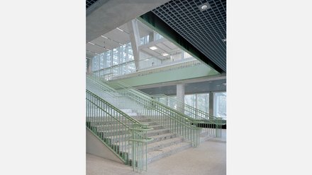 Helles Treppenhaus mit hellgrauen Steinstufen und hellgrünem Geländer. 