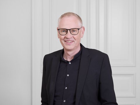 Mann mit Brille vor hellem Hintergrund.