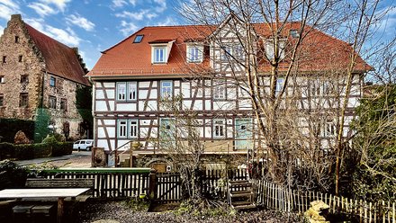 Fachwerkhaus Außenansicht mit Blick auf den Hof, der von einem Gartenzaun umzäunt ist.