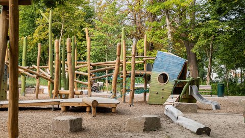 Spielplatz in einem Park mit Klettergerüst und Bäumen im Hintergrund