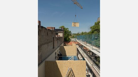 Ansicht einer Baustelle, im Hintergrund wird ein Bauelement von einem Kran transportiert