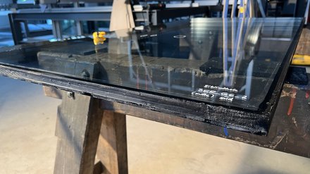 Mehrscheiben‑Isolierglas auf Werkstattböcken; schwarze Kantenversiegelung und Beschriftung sichtbar, Fokus auf Schichtaufbau der Glaskante.