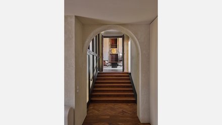 Gewölbter Durchgang mit Holztreppe und Blick in einen historischen Innenraum.