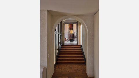Gewölbter Durchgang mit Holztreppe und Blick in einen historischen Innenraum.