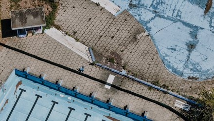 Luftaufnahme eines leerstehenden Freibads mit Becken, Wegen und Treppen.