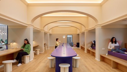 Heller Innenraum mit zentralem Tisch, Sitznischen und Personen beim Arbeiten.