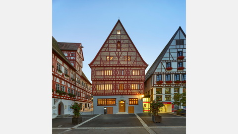 Fachwerkhäuser in der Altstadt von Oettingen, zwei Gebäude mit rotem Fachwerk und einem mittig beleuchteten Gebäude mit der Aufschrift ‚Krone‘.