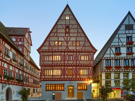 Fachwerkhäuser in der Altstadt von Oettingen, zwei Gebäude mit rotem Fachwerk und einem mittig beleuchteten Gebäude mit der Aufschrift ‚Krone‘.