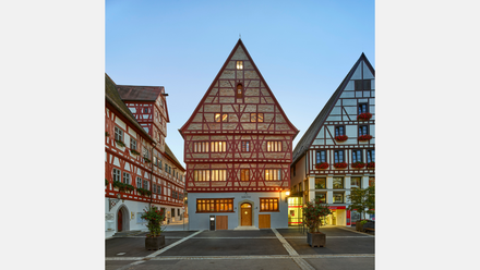 Fachwerkhäuser in der Altstadt von Oettingen, zwei Gebäude mit rotem Fachwerk und einem mittig beleuchteten Gebäude mit der Aufschrift ‚Krone‘.