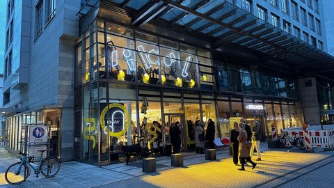 Abendliche Gesamtansicht eines Gebäudes mit transparenter Fassade und beleuchtetem Erdgeschoss.