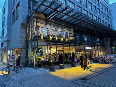 Abendliche Gesamtansicht eines Gebäudes mit transparenter Fassade und beleuchtetem Erdgeschoss.