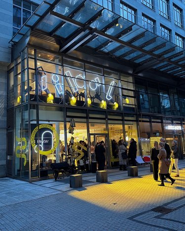 Abendliche Gesamtansicht eines Gebäudes mit transparenter Fassade und beleuchtetem Erdgeschoss.