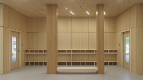 Heller Garderobenraum mit Holzverkleidung, zwei Holzsäulen, Sitzbank und mehreren offenen Fächern an den Wänden