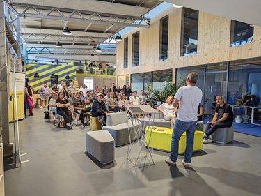 Redner spricht vor sitzendem Publikum in einer offenen, modernen Veranstaltungshalle.