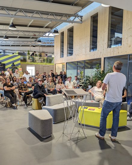 Redner spricht vor sitzendem Publikum in einer offenen, modernen Veranstaltungshalle.