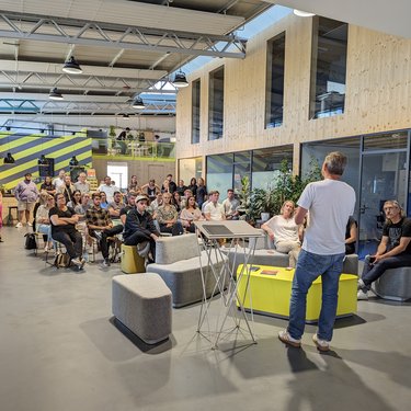 Redner spricht vor sitzendem Publikum in einer offenen, modernen Veranstaltungshalle.