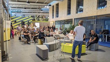 Redner spricht vor sitzendem Publikum in einer offenen, modernen Veranstaltungshalle.