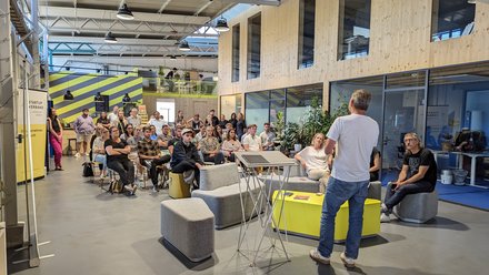Redner spricht vor sitzendem Publikum in einer offenen, modernen Veranstaltungshalle.