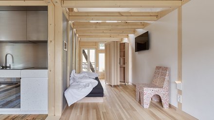 Ein minimalistisches Interieur eines Holzhauses mit einer Küche, einem Bett und einfacher Möbeln.
