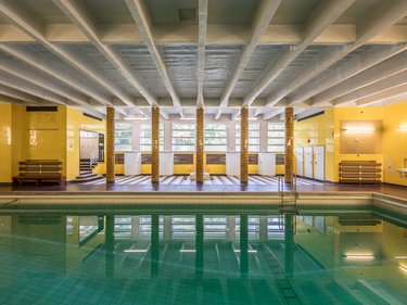Innenraum eines historischen Hallenbads mit Schwimmbecken.