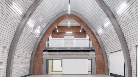 Heller Innenraum mit hoher, parabelförmiger Gewölbedecke aus Beton und Ziegel.
