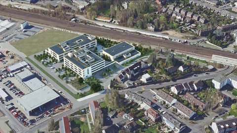 Luftaufnahme eines modernen Schulgebäudes mit Solaranlagen auf dem Dach, umgeben von Wohnhäusern und Bahngleisen