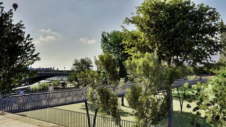 Eine Visualisierung zeigt einen erhöhten Fuß- und Radweg, der sich durch eine begrünte Parklandschaft schlängelt und an die Brücke anschließt, Menschen bewegen sich durch den baumbestandenen Raum, wodurch das Bild die Verbindung von Brücke, Park und Erholung sichtbar macht und für durchgängige Freiraum- und Bewegungsnetze steht.