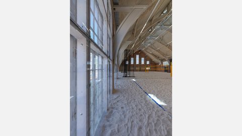 Innenansicht entlang großer Fensterfront mit Sandboden