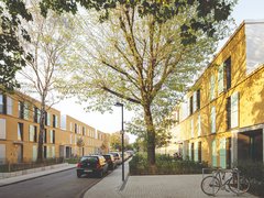 Ruhige Wohnstraße mit dichtem Baumdach; beidseitig zweigeschossige, ockerfarbene Reihenhäuser mit mintgrünen Fensterläden; geparkte Autos und ein Fahrradständer auf breiten Gehwegen im Schatten.