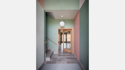 Schmaler Flur mit grün gestrichenen Wänden, Fliesenboden und Blick auf eine verglaste Tür am Ende.