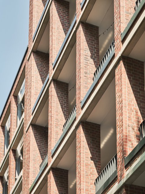 Fassade eines mehrstöckigen Gebäudes mit roten Ziegeln und vertikalen Betonstreben