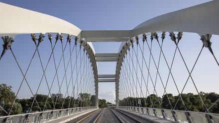 Zentrale Perspektive über die Gleise einer Eisenbahnbrücke mit weißem Stahlbogen und Seilkonstruktion.