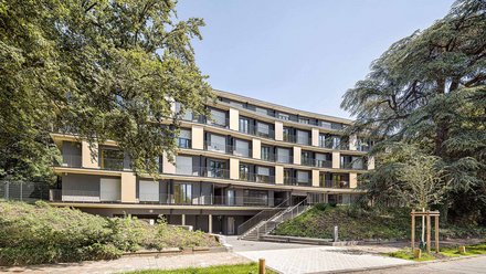 Ein Wohnunhaus zwischen zwei grünen Bäumen. 