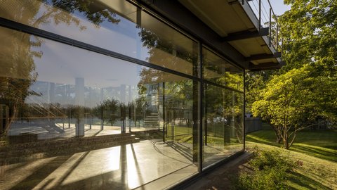 Moderne Glasfassade eines Gebäudes mit Spiegelung von Bäumen und Schatten auf dem Boden
