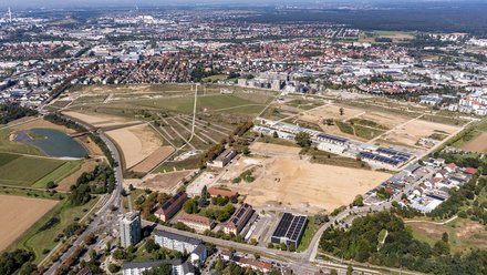 Luftaufnahme eines Entwicklungsgebiets, große Freiflächen, Baustellen, Wege und angrenzende Stadtstruktur.