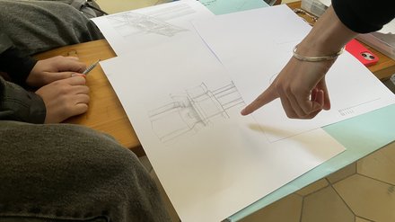 Architektonische Zeichnung auf einer Bank. Eine Hand zeigt auf die Skizze 