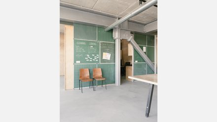 Innenraum mit grünen Tafel-Paneelen voller Notizen, zwei Holzstühle an der Wand; sichtbare Stahlträger.