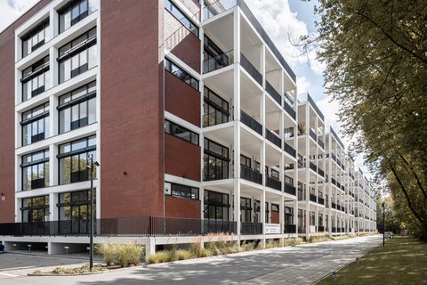 Moderner mehrstöckiger Bürokomplex mit großen Fenstern und Balkonen an einer Baumallee