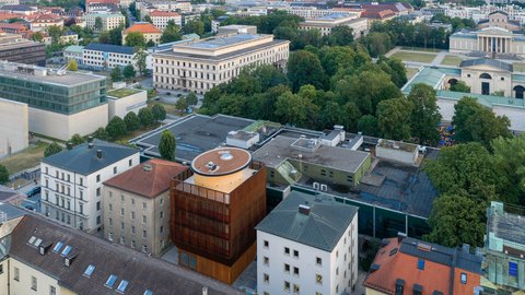 Luftaufnahme eines Stadtviertels mit mehreren Gebäuden, einem großen Park und einer weitläufigen Stadtlandschaft im Hintergrund
